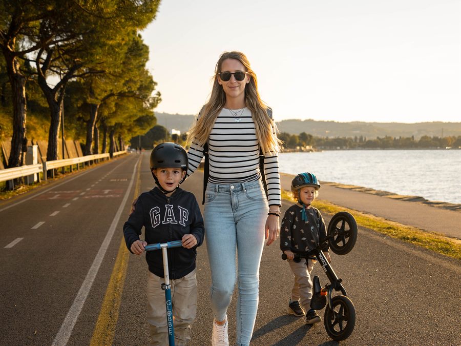 A mother and her two children on scooters by the water