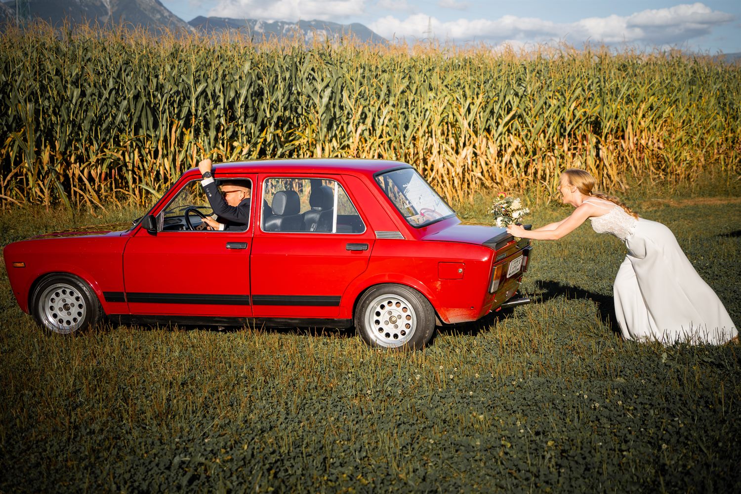 The bride beside a red car in front of a maize field