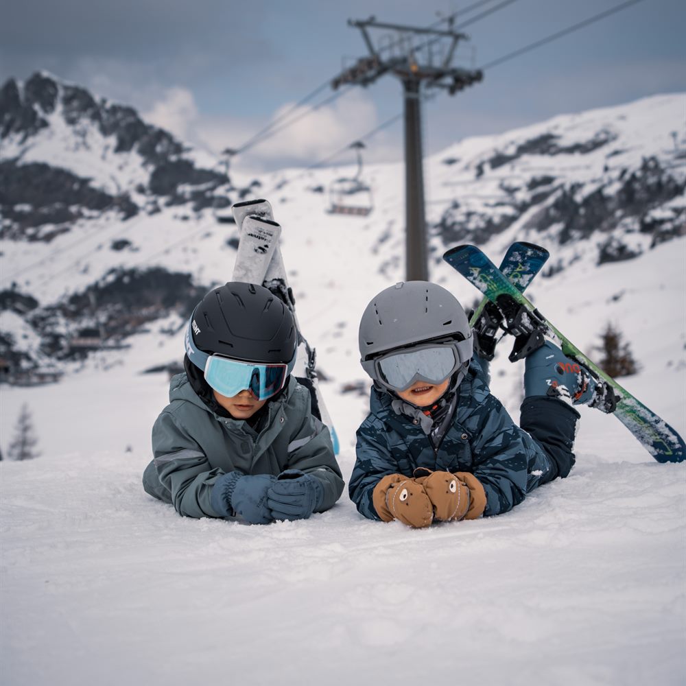 Two children lying in the snow with their skis